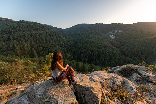 A young woman hiking in Kazdağı (Kaz Mountain) National Forest Park is resting on high rock.