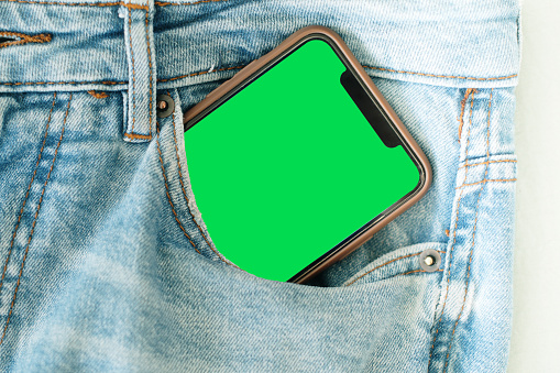 A partially visible smart phone with green screen inside a jeans pocket