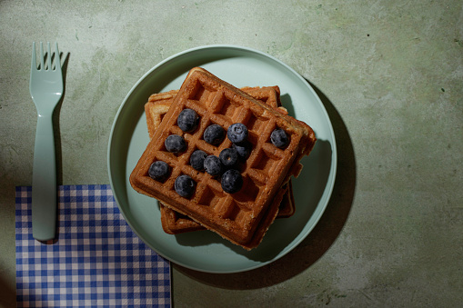 Two waffles with blueberries on a green plate