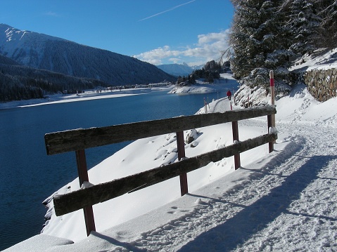 walk around the lake in the canton of graubünden. winter landscape with lake and in the background mountains and a village. walking in the snow