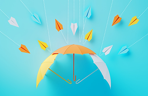 Colorful umbrellas establishing a shield against paper planes coming at different directions on blue background. Horizontal composition.