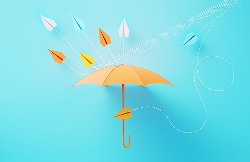 Colorful umbrella establishing a shield against paper planes coming at different directions on blue background. Horizontal composition.