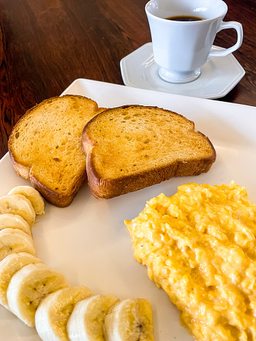 a white square plate for breakast with eggs, bananas and toast bread on a wooden table background