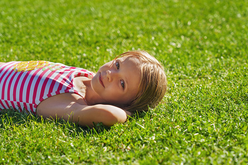 A little girl lies on the meadow in the sunlight.