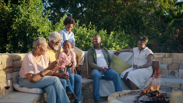 Happy family, together and love in garden fire for bonding and clapping hands for celebration on holiday. African people, generations or sharing of elderly wisdom with talking or reunion on vacation