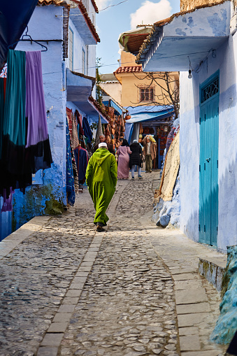 Narrow shopping street with man walking in green djellaba in blue city of Chefchaouen, Morocco, North Africa.