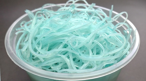 Blue plastic noodles in a plastic container on a gray background, top view