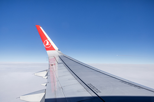 Airspace above Eastern Europe - January 3th 2024:  Wing and winglet of an Airbus 320 from Turkish Airlines above the skies against the blue sky and a passing passenger plane going the opposite way