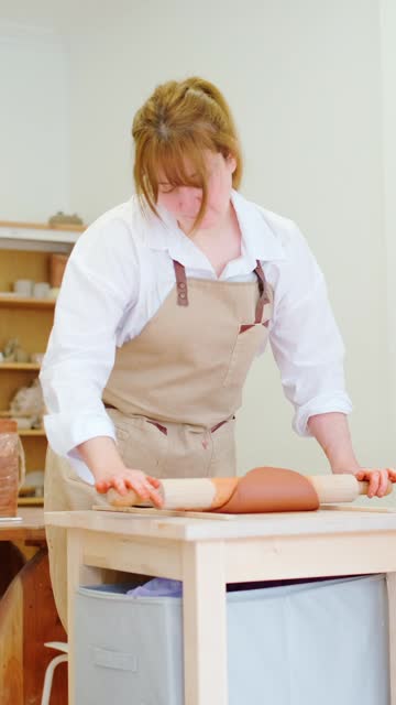 Woman kneading mud with a rolling pin in a workshop