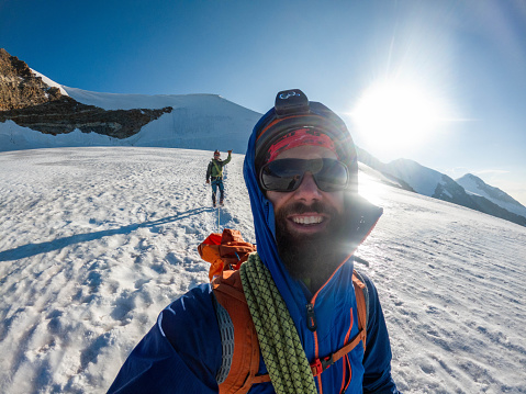 Radiant with triumph, a team of mountaineers descends from the summit, seizing the moment for a celebratory selfie amidst the breathtaking landscapes of their victorious descent.