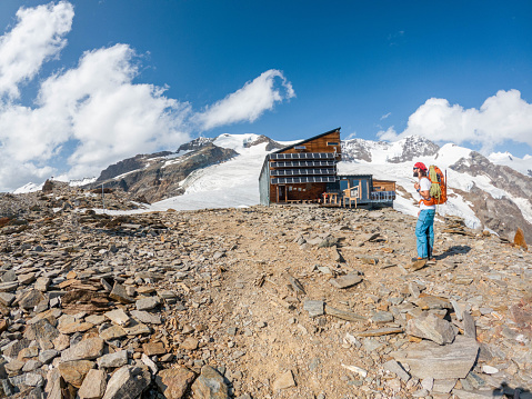 A resilient mountaineer reaches a mountain hut nestled in the Swiss Alps, a haven amid the majestic peaks, marking the end of an adventurous ascent.
