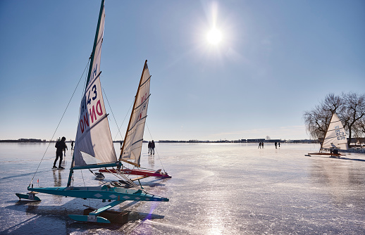 Ice sailing on the Braassemermeer near Roelofarendsveen in the municipality of Kaag en Braassem mede Veendermolen on a sunny day. It is mid-February 2021 in the Netherlands, people are skating and ice sailing on a large lake.
