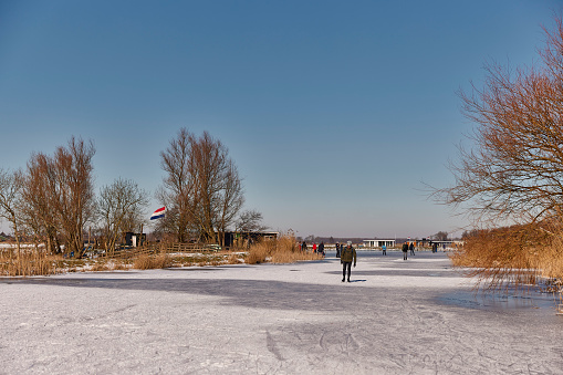 Ice skating on the narrow waters in the Netherlands near Roelofarendsveen in the municipality of Kaag en Braassem mede Veendermolen on a sunny day. It is mid-February 2021 in the Netherlands.