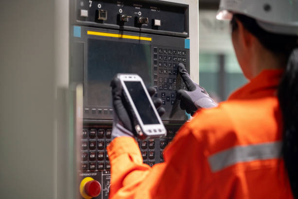 istock Asian supervisor takes charge at the CNC machine's control panel. Supervisor orchestrates efficiency and precision as they press a button to initiate the automated system. Dressed in safety attire, complete with a hardhat and reflective clothing 2063261055