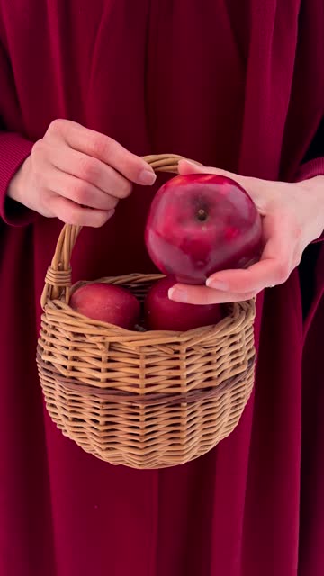 Vertical: A woman holds a basket of red apples in the style of Red Hood