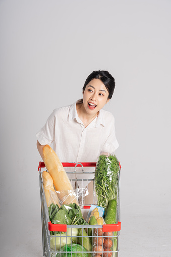 Smiling woman happily pushing a supermarket cart, isolated on white background