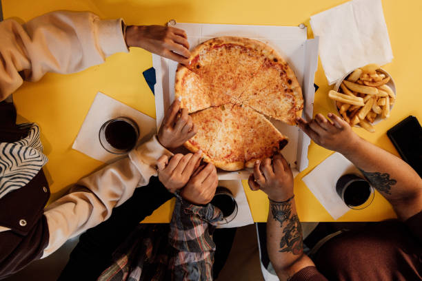 Three friends eating pizza slices at home directly above view.