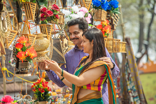 Happy mid adult husband and wife buying wicker decorations at market stall while doing shopping at Surajkund fair