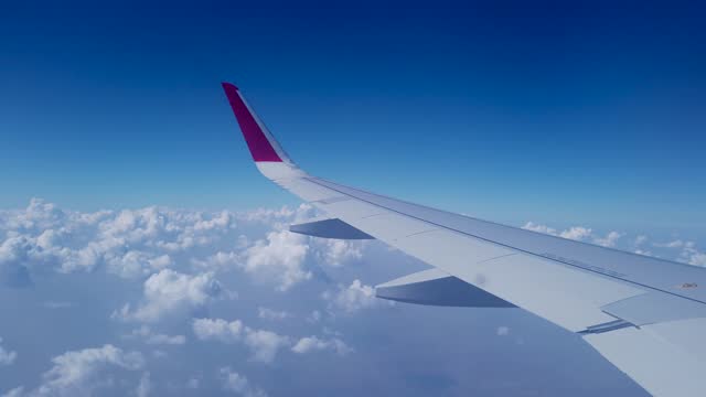 A Window view of an Aero plane wing gliding above the white clouds through the vibrant blue Sky in India.