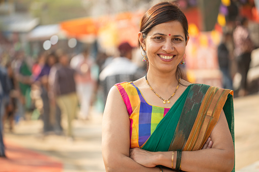Portrait of smiling beautiful mid adult woman dressed in sari with arms crossed standing in street market at Surajkund fair