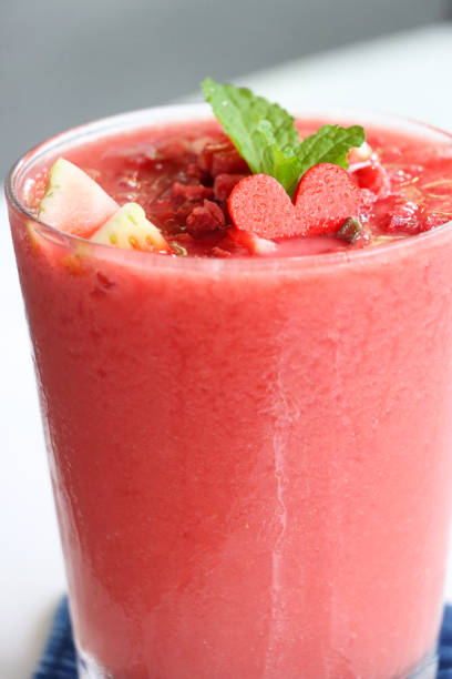 Stock photo showing close-up view of drinking glass filled containing strawberry and watermelon juice smoothie as part of a healthy breakfast.