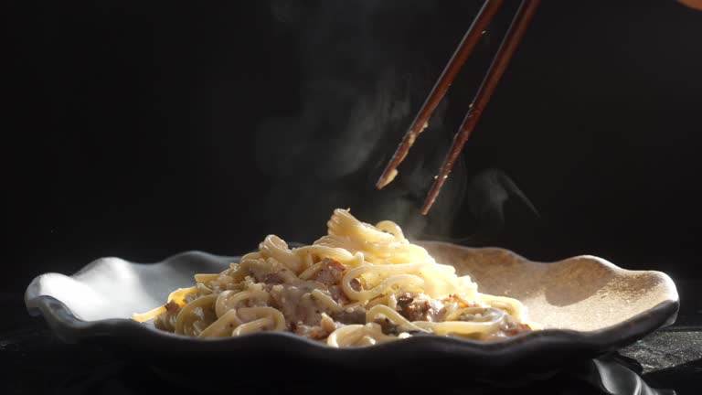 The steam from spaghetti with cream sauce. The woman's hand is eating carbonara which is made with eggs, hard cheese, cured pork, and black pepper. Italian food on a white smoke background.