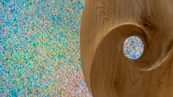 Wooden block with shape and hole through which you can see the colours of the background, abstract