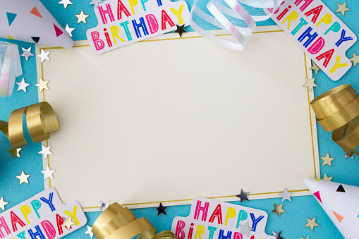 A blank party invitation with copy space, surrounded by happy birthday confetti, party hats, ribbons and stars .