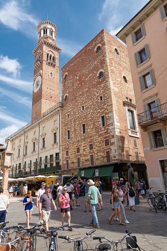 Verona, Italy – August 01, 2023: Tourists on the Piazza delle Erbe with the Torre dei Lamberti bell tower in the old town of Verona in Italy
