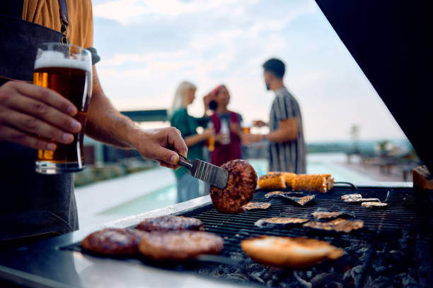 primer plano de un hombre que prepara una barbacoa mientras se reúne con amigos. - cocido a la parrilla fotografías e imágenes de stock