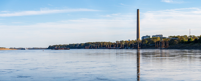Large barges pass in front of New Madrid power station in Missouri on the Mississippi river in broad panorama