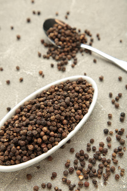 istock Black pepper corns in white plate on grey concrete background. Vertical photo 2063456925