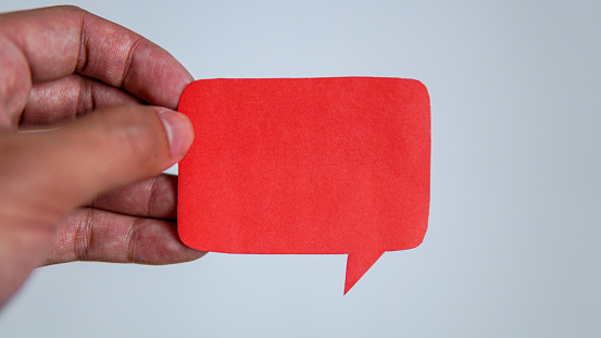 Man's hand holding a red message speech bubble. Man conveying important information with paper speech bubble.