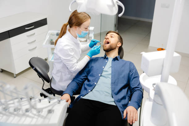 a handsome man is sitting in a chair at a woman's appointment at the dentist's office - zahnpflege stock-fotos und bilder
