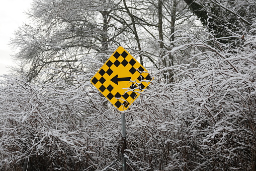 Hazard ahead, turn left directional sign. Edge of a forest in Metro Vancouver, Canada.