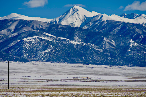 Snow-covered mountain peaks of the Sangre de Cristo range dwarf a farm in the upper San Luis Valley in Saguache County, Colorado, on a sunny winter day.