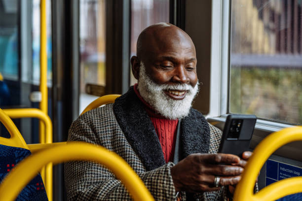 Senior African man using public transport and text messaging on smart phone device