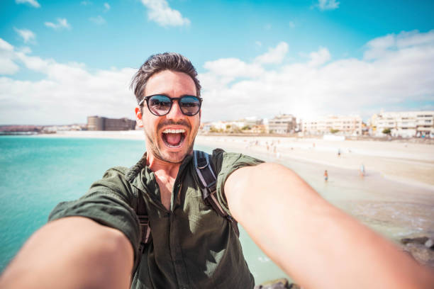 istock Handsome young man taking selfie with smart mobile phone device outside - Cheerful tourist enjoying summertime at the beac 2063563599