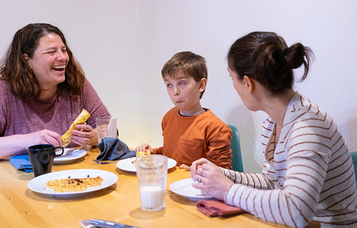 Family of two lesbian mothers and their son having breakfast together at home while the boy makes faces and laughs