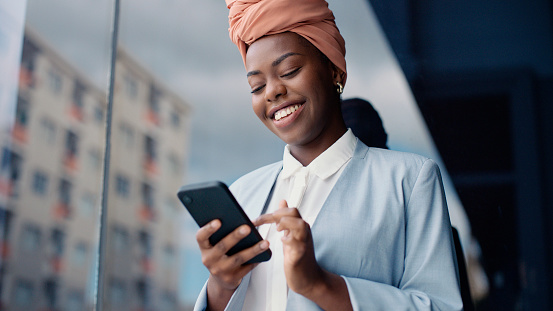 Black business woman, phone and happy in city for texting, thinking or laugh at meme on web. Person, employee and reading in street by buildings with smartphone for mobile app, chat or social media