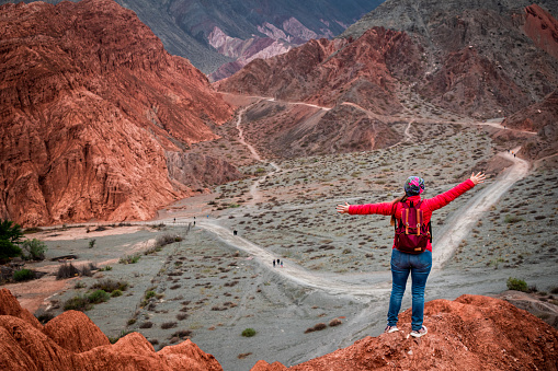 Tourist with arms outstretched in front of the beautiful and colorful mountain in Purmamarca, Jujuy, Argentina. Young woman on vacation in Purmamarca, Jujuy, Argentina. Young woman traveling through northern Argentina.