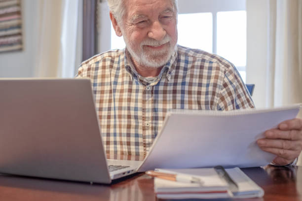 istock Smiling bearded man sitting at table with laptop and books working or studying. Attractive senior man enjoying teaching activity and learning using new technology 2063659216