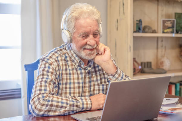 istock Video call concept. Smiling bearded man sitting at table with laptop and books working or studying in video connection. Attractive senior man enjoying teaching activity and learning using new technology 2063661340