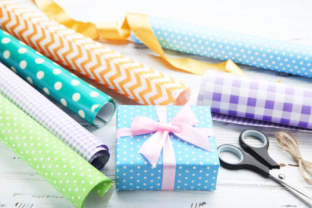 Rolls of craft papers with gift box and scissors on white wooden background