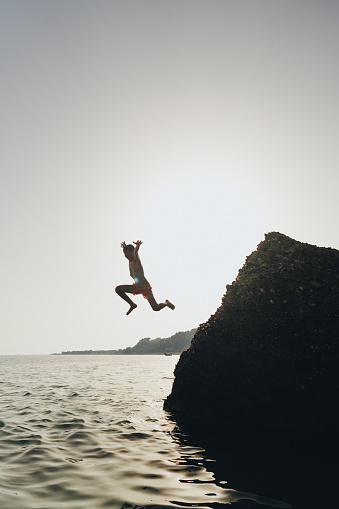 Photo of an adventurous young boy jumping off a big rock into the sea