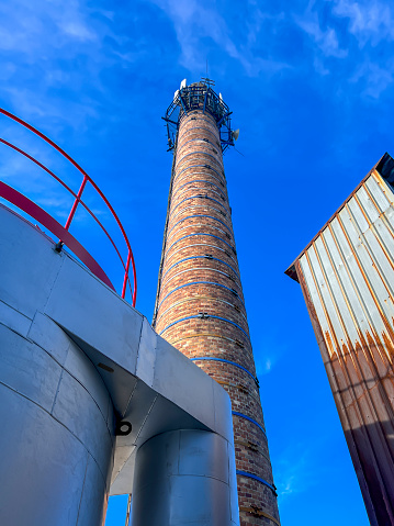 An old ceramic chimney (made of brick) and an old and new flue gas dust collector behind a coal boiler, a grate, against the blue sky.