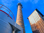 An old ceramic chimney and an old and new flue gas dust collector behind a coal boiler, a grate, against the blue sky.