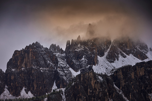 Mountain peaks covered with the first snow of the year, Dolomites Alps, Trentino Alto Adige, Italy. The sun shines a little through the clouds.