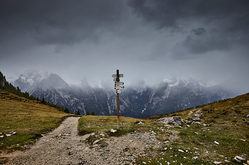 Path sign Dolomites Alps, Italy during a grey day. The snow is still falling. In the back you see the mountains in the clouds.