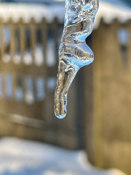 Extreme close-up of a drop of water at the end of Ice hanging from a roof on a cold, winter evening in Colorado at sunset.